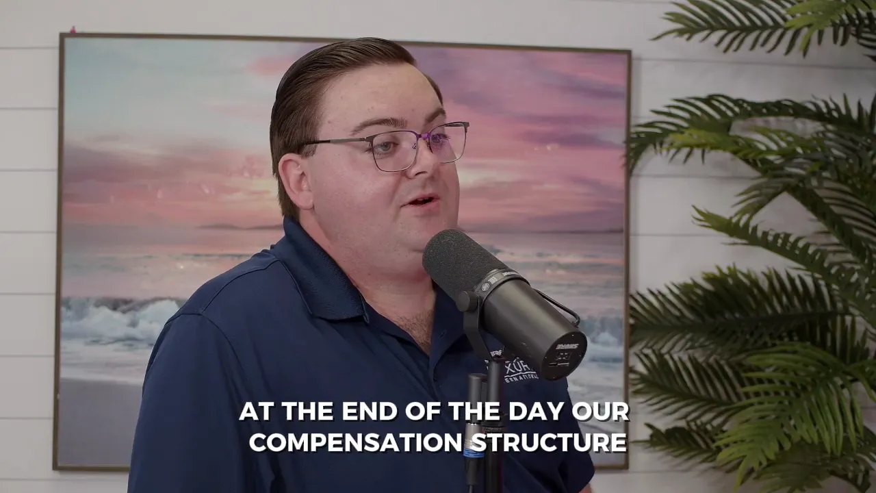 Person speaking into a podcast microphone with a framed beach painting behind them and on-screen subtitle 'AT THE END OF THE DAY OUR COMPENSATION STRUCTURE'.