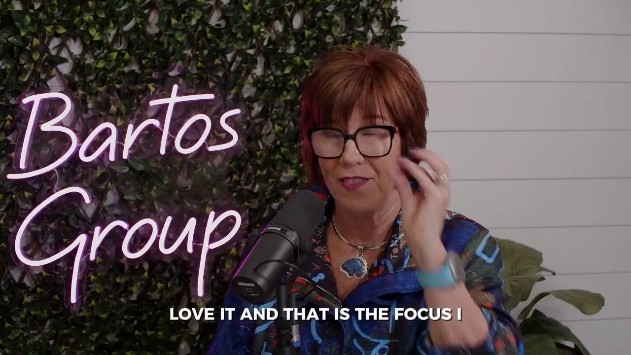 Woman speaking into a microphone in front of a neon 'Bartos Group' sign and greenery; on-screen subtitle reads 'LOVE IT AND THAT IS THE FOCUS I'.